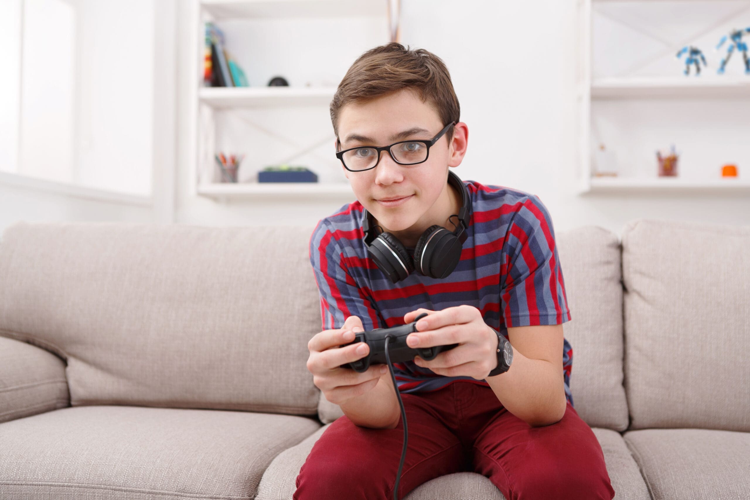 Gaming video games concept - teenage boy playing football game with joystick and headphones, enjoying sitting on sofa in living room at home
